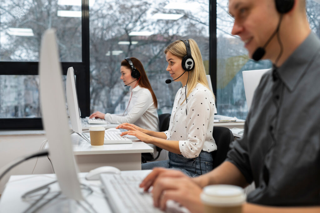 Three people wearing headsets working at computers in an office.
