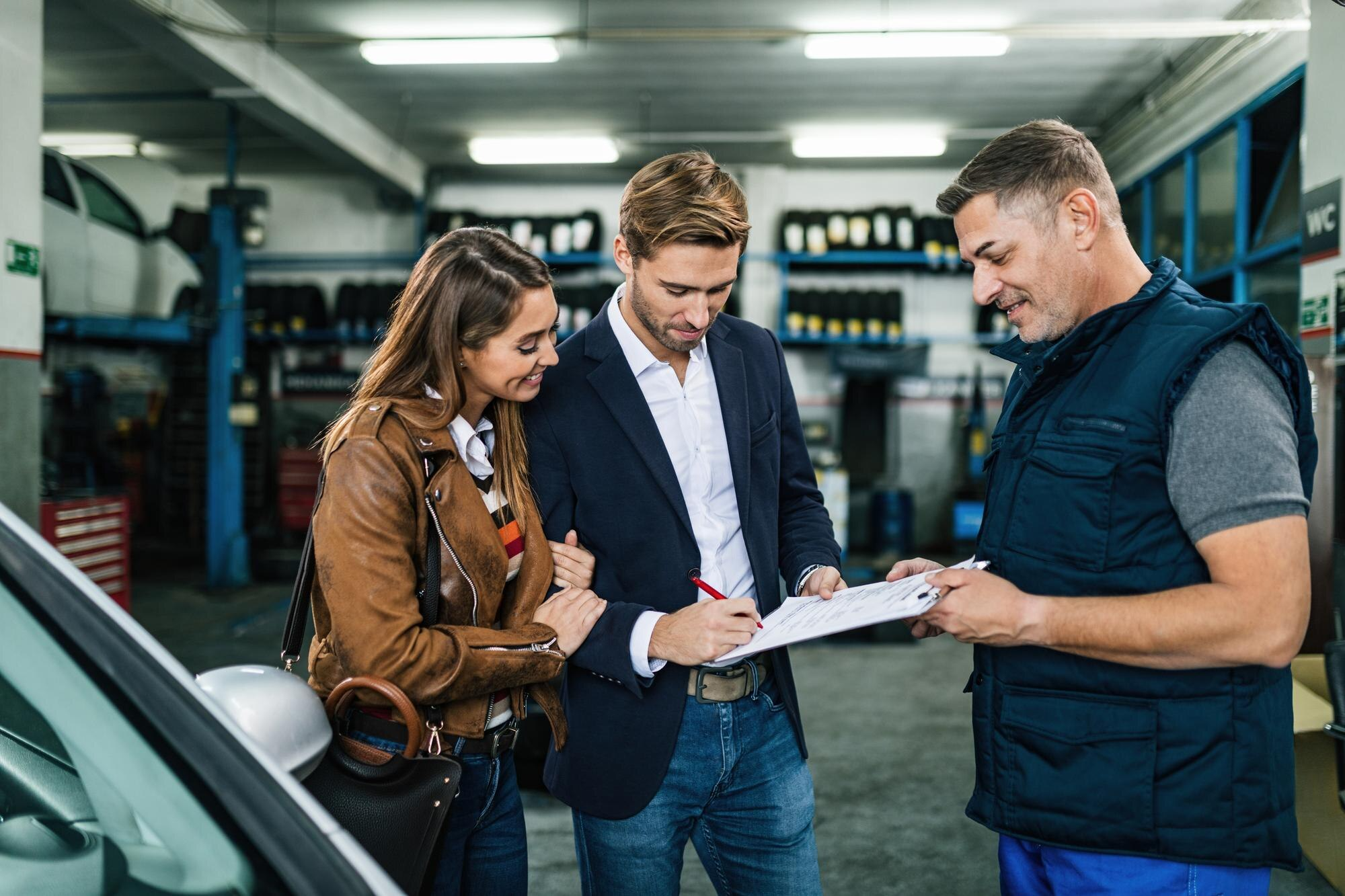 Man and woman looking at document with mechanic in garage.