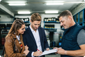 Three people looking at a document in a warehouse setting.
