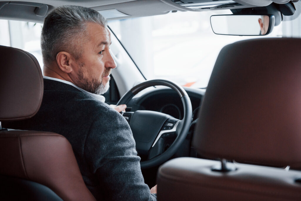 Man in a gray coat driving a car with brown leather seats.